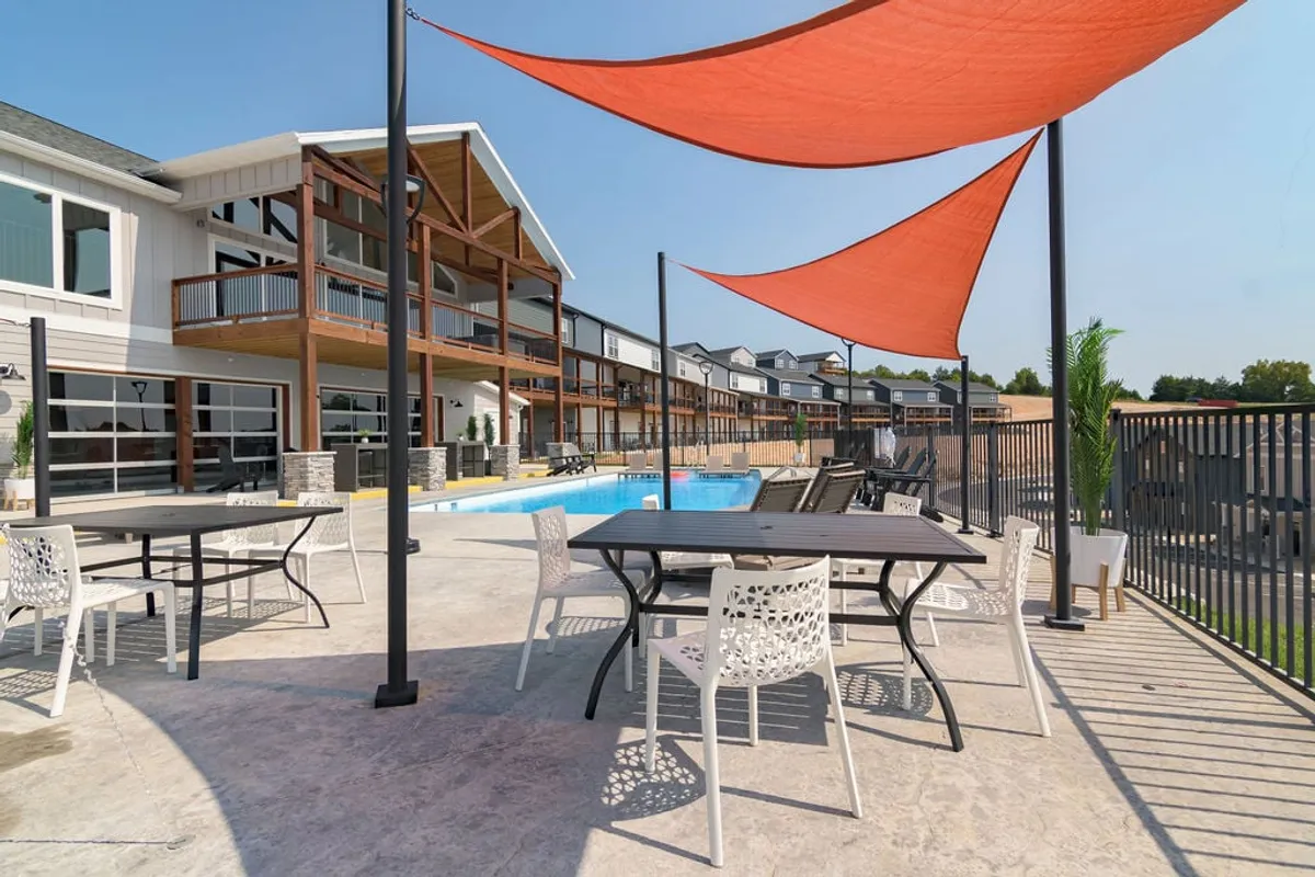 An exterior view of a swimming pool area with outdoor seating, decorative shade sails, and modern architecture. The space is designed for social gatherings and relaxation, with clear appeal for evening events and group leisure after exploring the city.