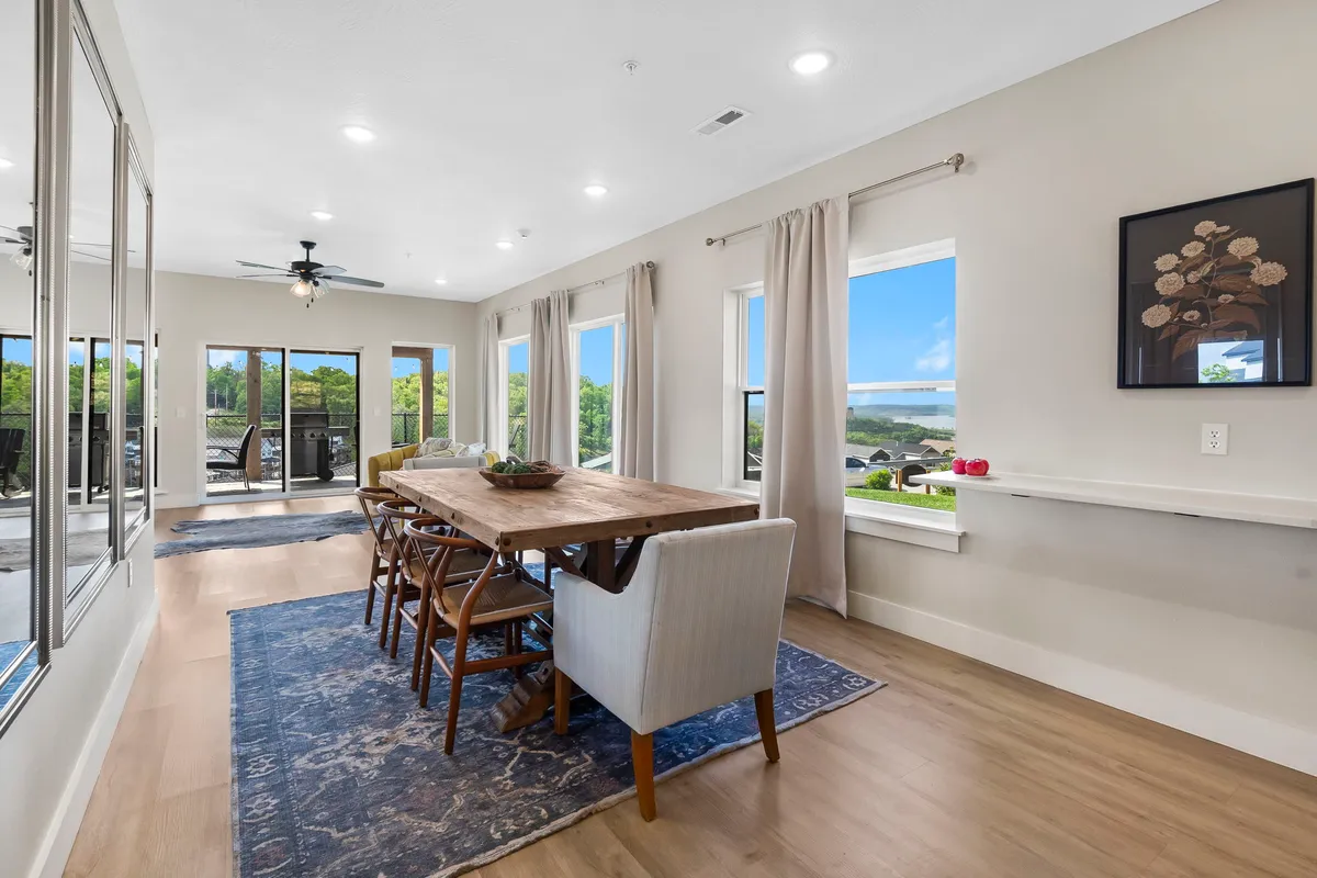 A spacious dining area with a large wooden table, surrounded by comfortable seating and set before expansive windows. Decorative touches such as a mirror and area rug enhance the cozy atmosphere. The windows frame beautiful natural views, echoing the mountain and lake scenery described in the section.