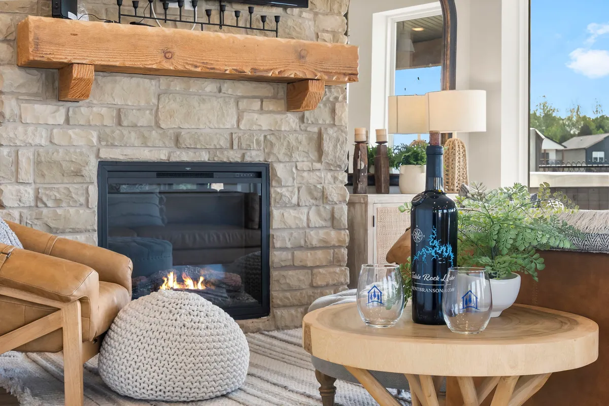 A close-up of a cozy nook with a stone fireplace and a wooden mantel, featuring a soft armchair and a coffee table set with wine and glasses. The scene conveys comfort, warmth, and opportunities for intimate gatherings or quiet relaxation by the fire.