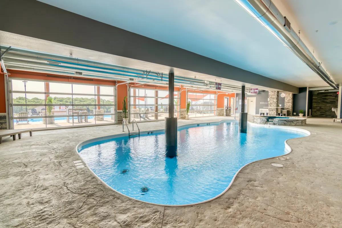 A modern indoor pool scene with tranquil blue ceilings, expansive windows, stylish lighting, and a serene swimming area. The design feels inviting and fresh, ideal for swimming or lounging regardless of the weather outside.