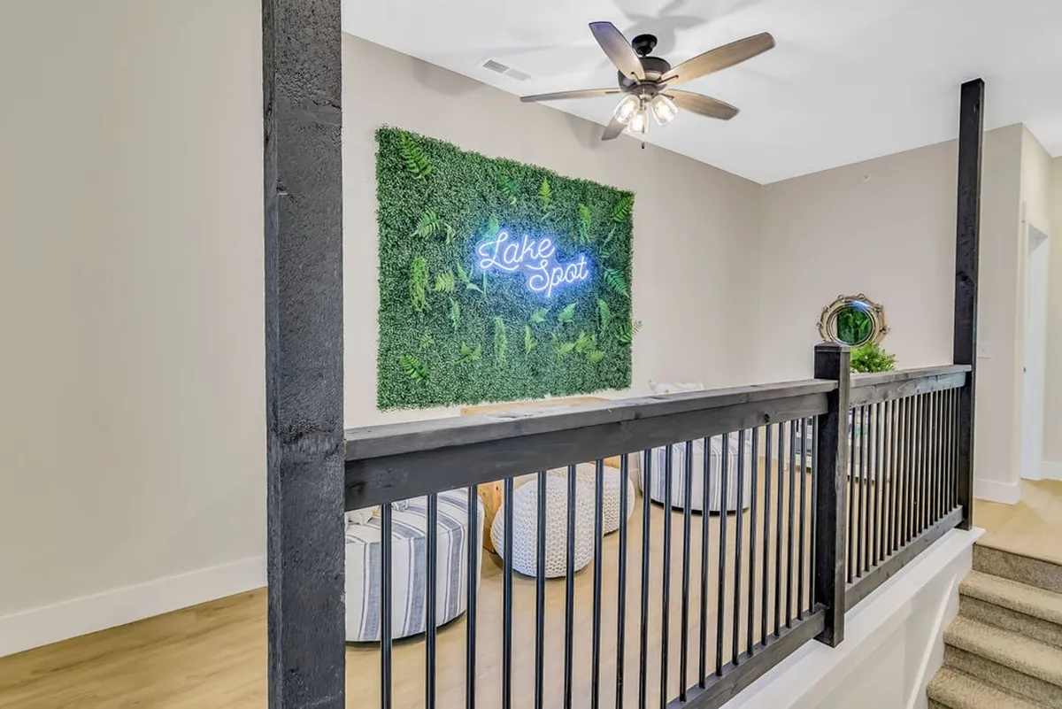 A playful kids’ hangout zone with a neon 'Lake Spot' sign, a lush green wall, bean bag chairs, and a ceiling fan overhead. The room’s bright accents and casual seating make it perfect for play, dance, or socializing.