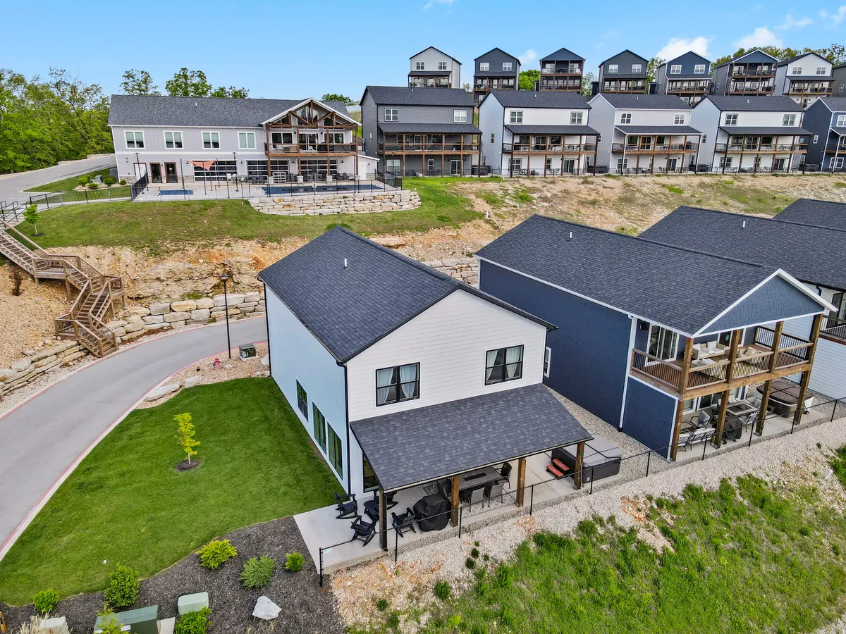 This exterior shot highlights a modern two-story house surrounded by greenery, with a stone path, porch, and neighboring homes in view. The scene captures a communal neighborhood vibe, hinting at proximity to local attractions, shops, and social venues.