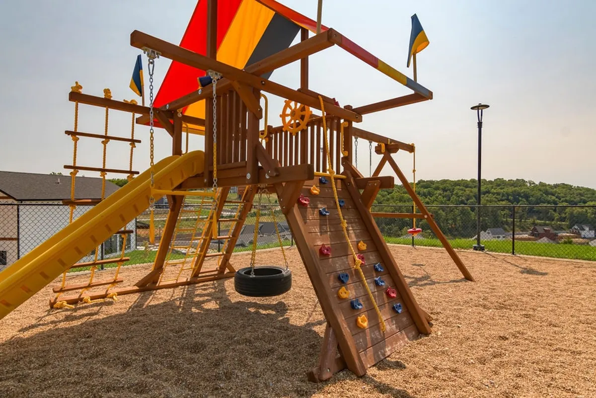 A lively and colorful playground featuring a climbing wall, slide, tire swing, and cheerful flags. The setting is bright and inviting, designed to spark children’s imagination and active play.