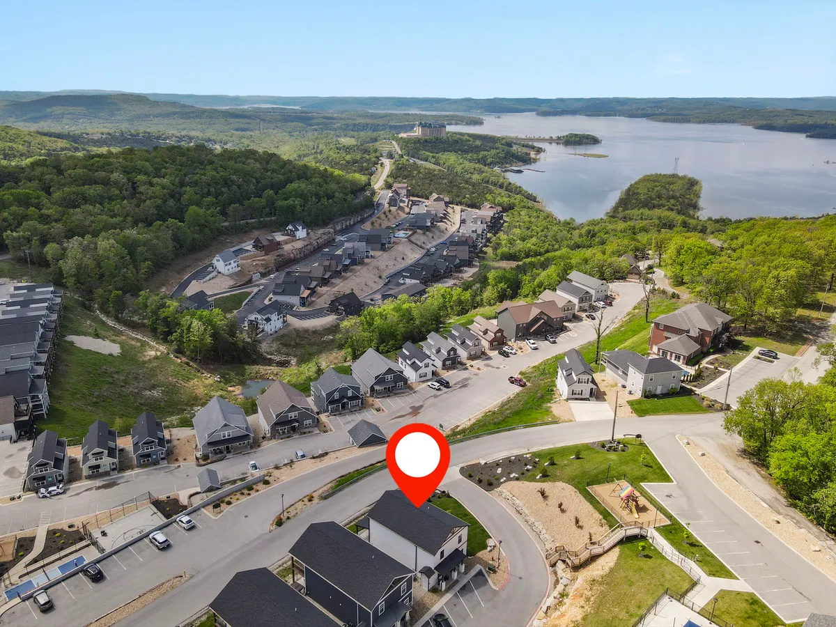 An aerial exterior view showing a tranquil water body surrounded by lush hills and a glimpse of the neighborhood layout. The inviting landscape is suited for boating, hiking, and family gatherings, with the water’s edge and community spaces visible.