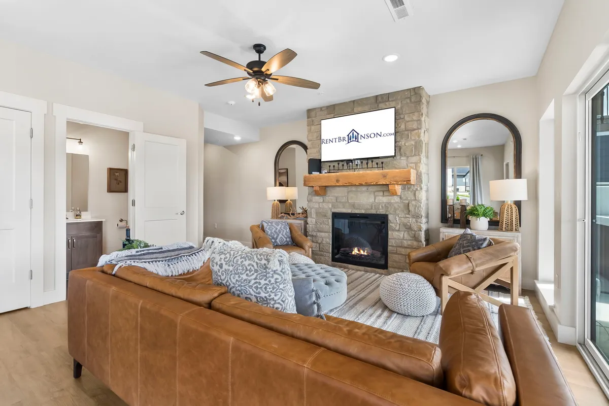 A warmly lit living room featuring a stone fireplace as the centerpiece, flanked by a leather sofa adorned with decorative pillows. A TV is mounted above the fireplace, and a coffee table sits in front, inviting guests to gather, relax, or enjoy movie nights together.