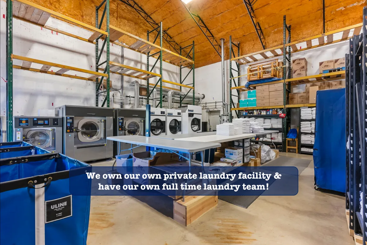 This image reveals a behind-the-scenes look at a spotless, professional laundry facility with industrial laundry machines, folding tables, and laundry carts. The environment is efficient and organized, underscoring the commitment to cleanliness and high-quality linen care.