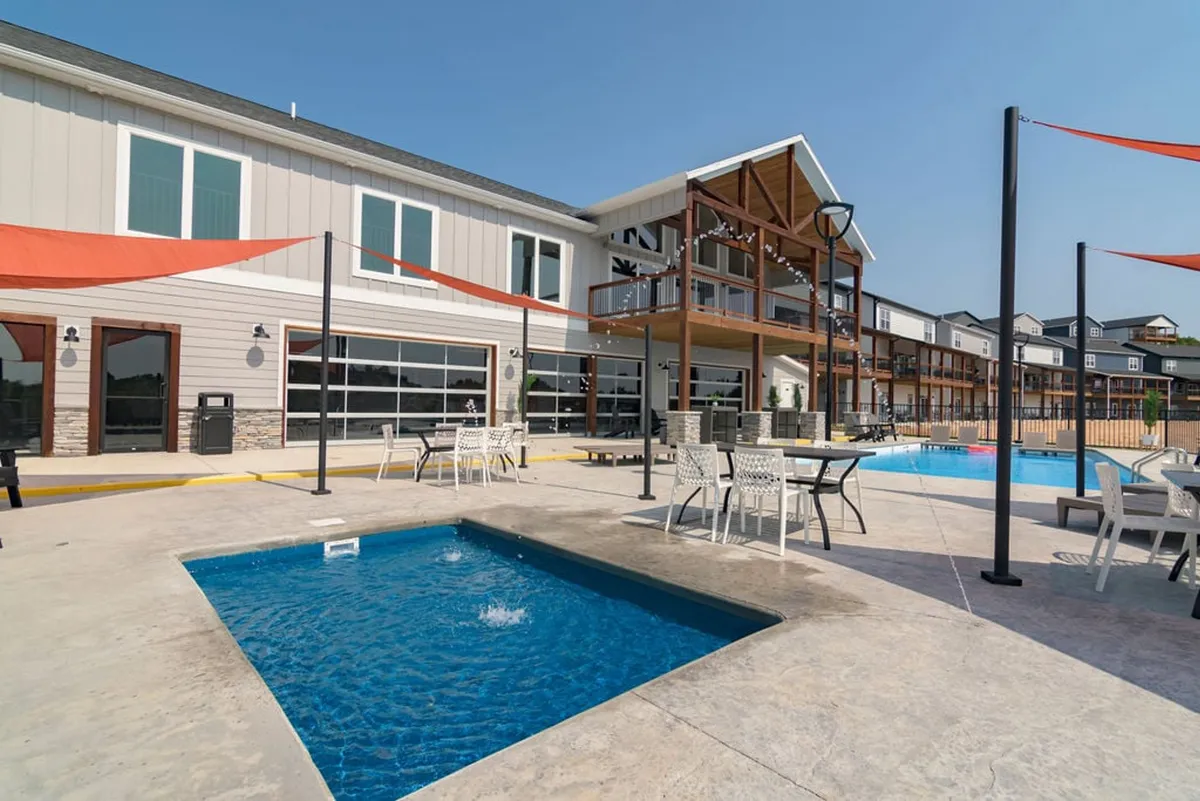 This image showcases a community outdoor swimming pool, a hot tub, and various outdoor seating areas, with the backdrop of a modern building facade. The environment is lively yet relaxed, ideal for swimming, sunbathing, and gathering with friends or family.