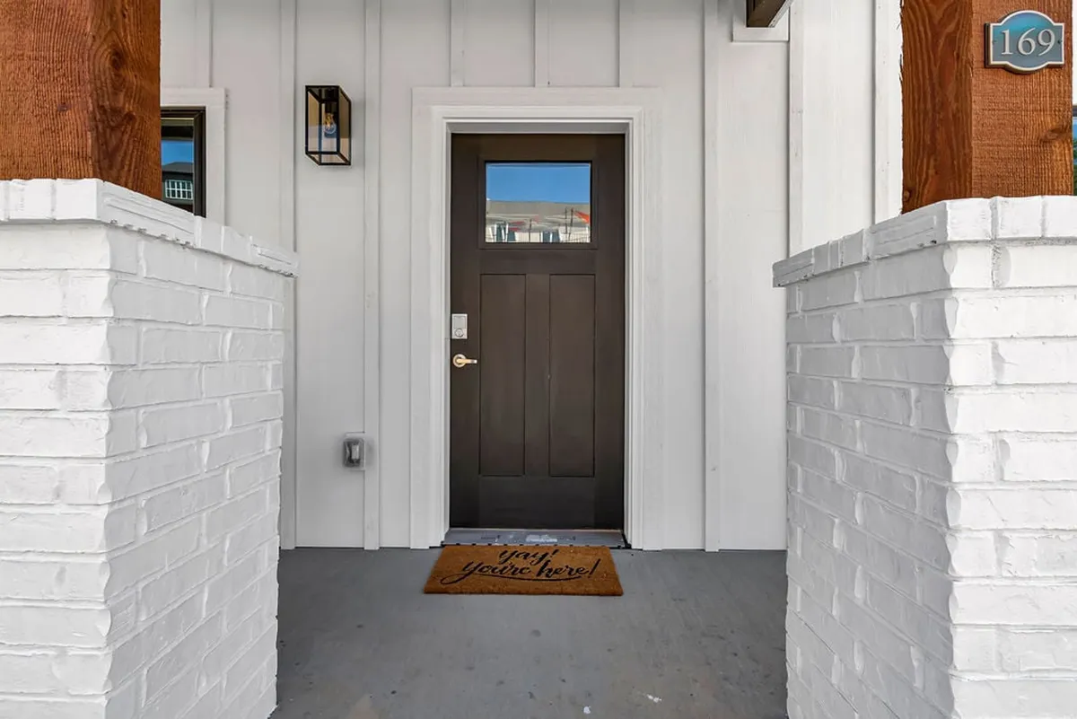The image captures a welcoming entrance with a pristine front door, a clean welcome mat, and stately brick columns. The composition conveys a sense of arrival and the importance of first impressions in a well-maintained property.