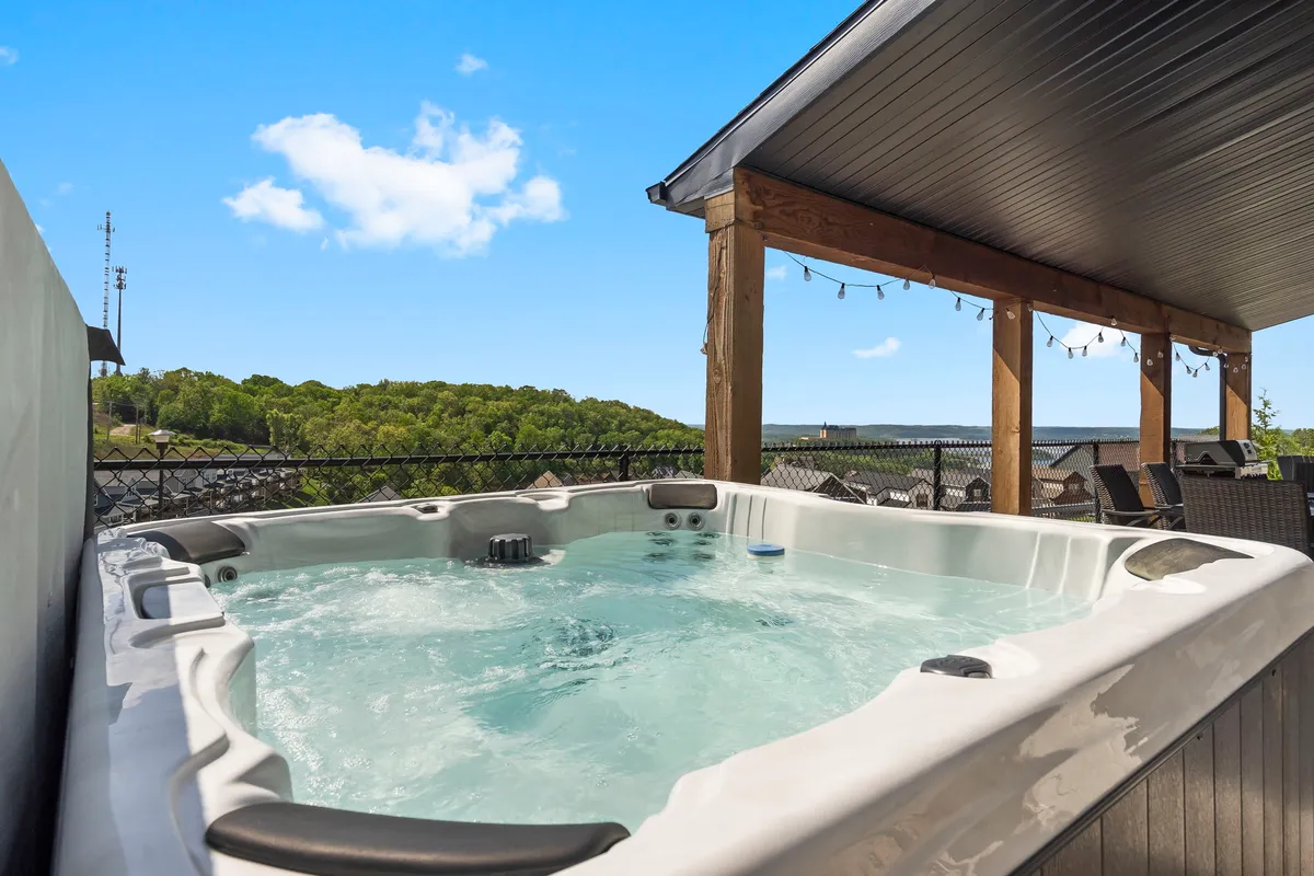 An exterior view of a hot tub set on a deck with scenic natural surroundings, complemented by inviting outdoor seating and string lights, suggesting relaxation after a day of adventure.