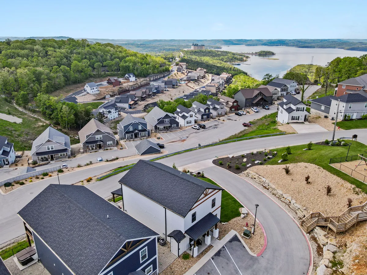 A wide view featuring a peaceful lake nestled among rolling green hills, with modern homes and a meandering road in the foreground. The scene exudes a sense of community and is perfect for outdoor activities like walking, cycling, and engaging in water sports.