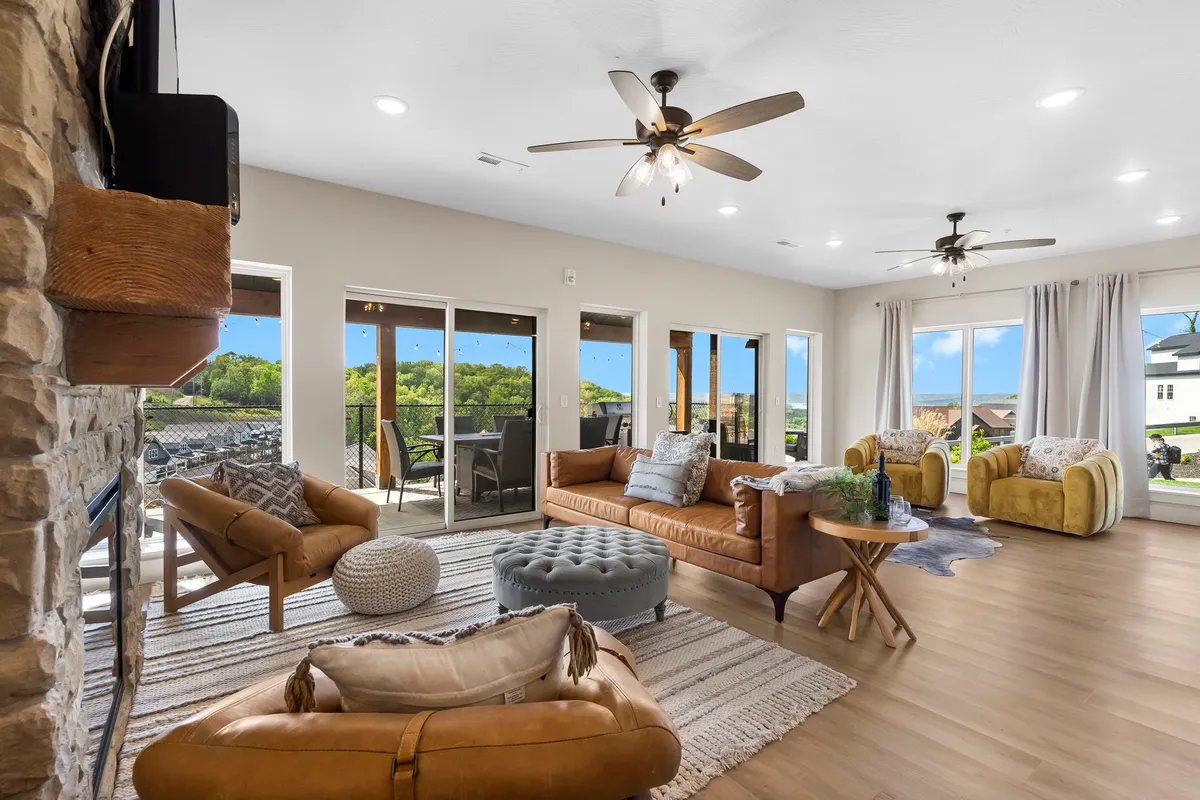 The image showcases a bright, inviting living room featuring a plush, comfortable sofa and stylish accent chairs arranged around a decorative coffee table. Large windows frame a beautiful view, flooding the space with natural light and offering guests a glimpse of the surrounding scenery. The setup suggests a perfect spot for relaxing mornings, lively family gatherings, or cozy evenings together.